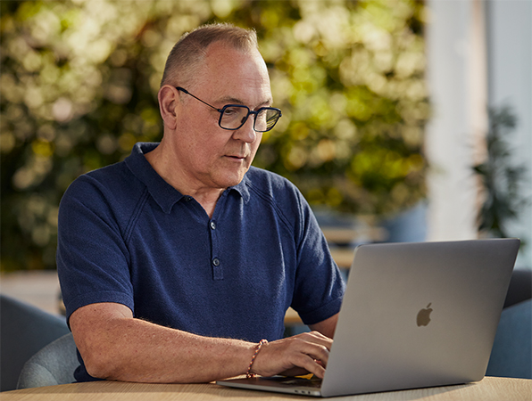 一位 Apple 軟體和服務團隊的員工正在戶外使用 MacBook 工作，背景中有綠色植物。