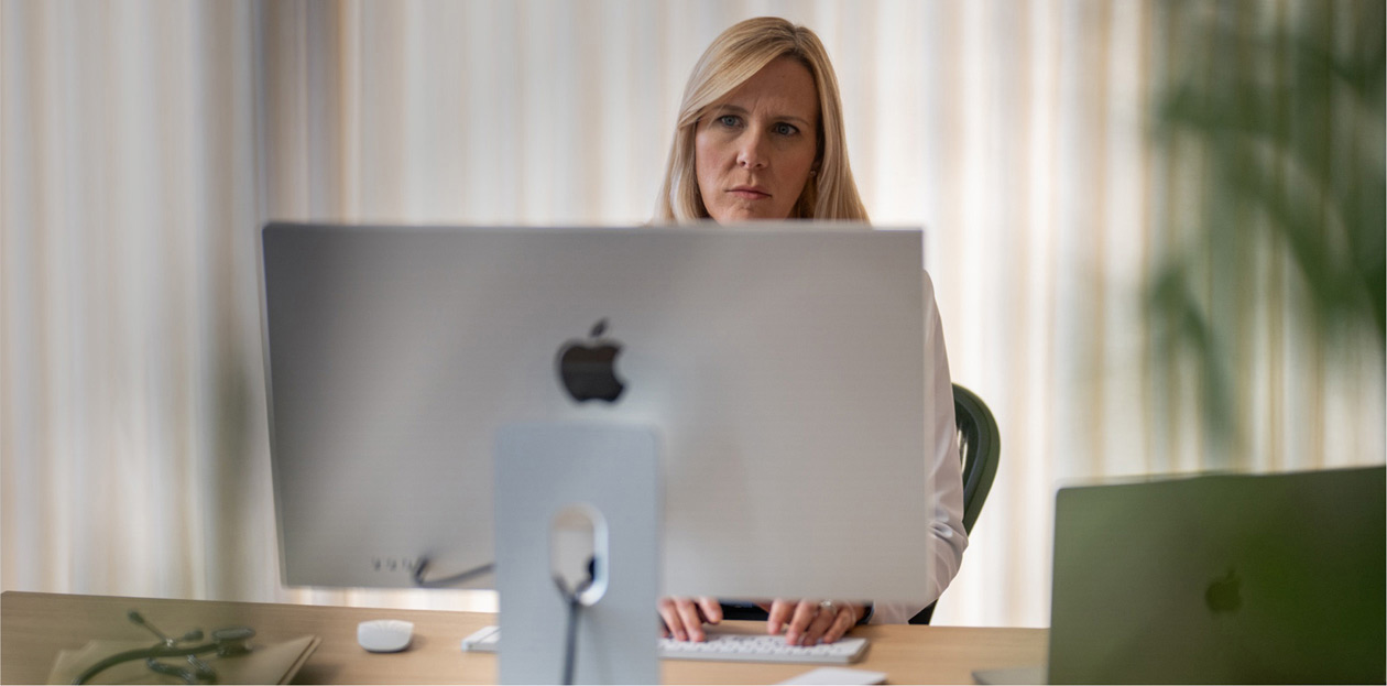 Een zorgverlener kijkt van achter haar bureau naar een iMac-scherm.