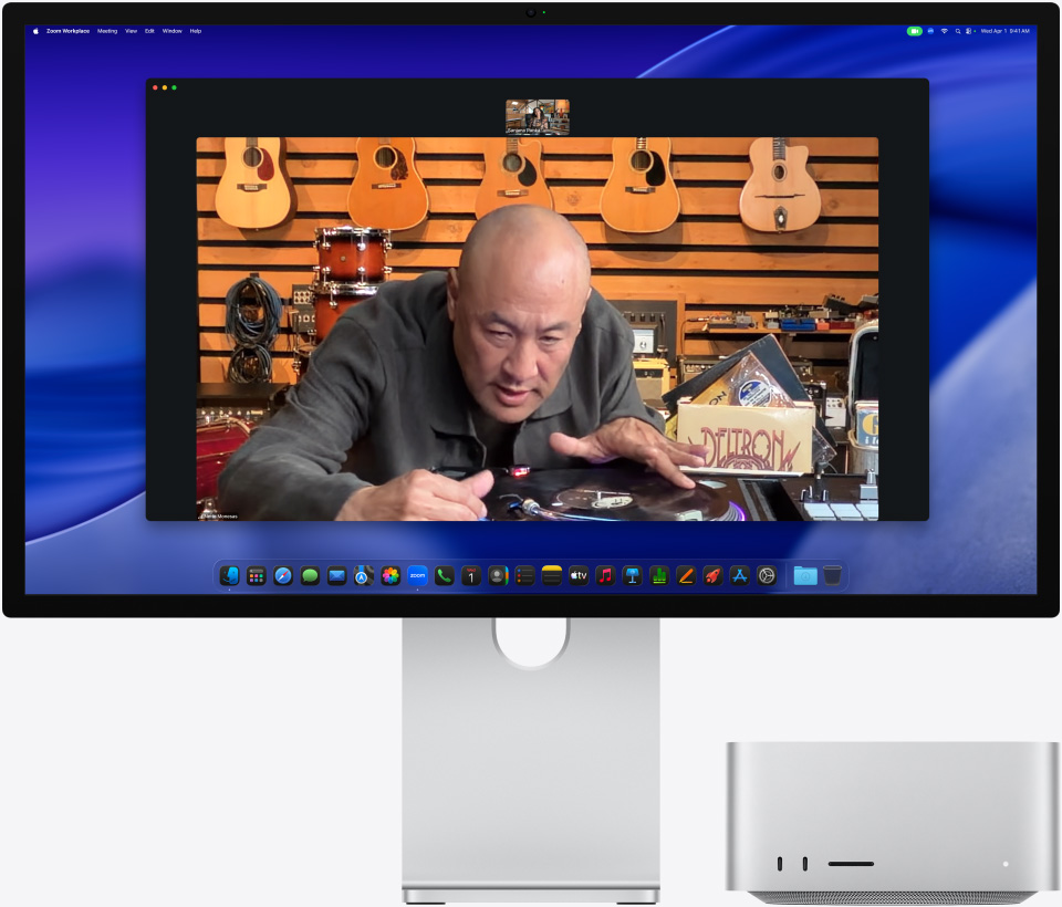 Osoba w sklepie muzycznym przygląda się uważnie gramofonowi podczas wideorozmowy na monitorze Studio Display XDR, pod którym umieszczony jest Mac Studio