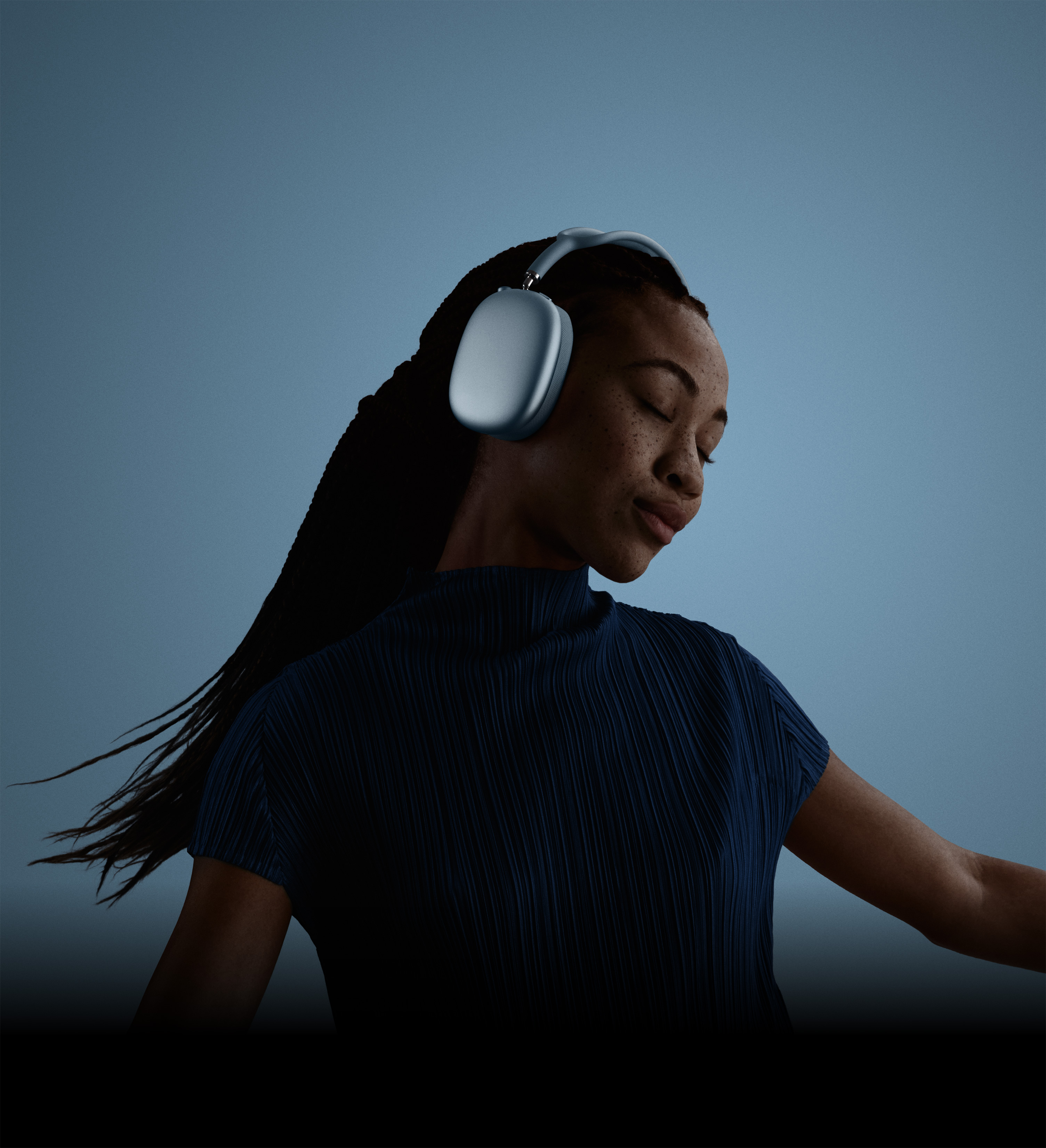 Suletud silmade ja kallutatud peaga inimene külgvaates, kandes sinist tooni AirPods Max 2 kõrvaklappe.