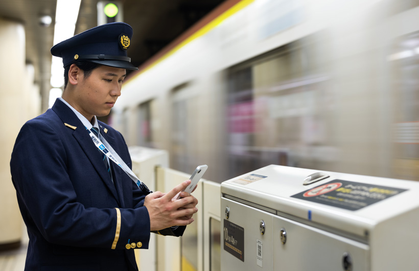 Un agent de station se tient sur le quai et balaie un code QR avec son iPhone pendant qu’un train passe.