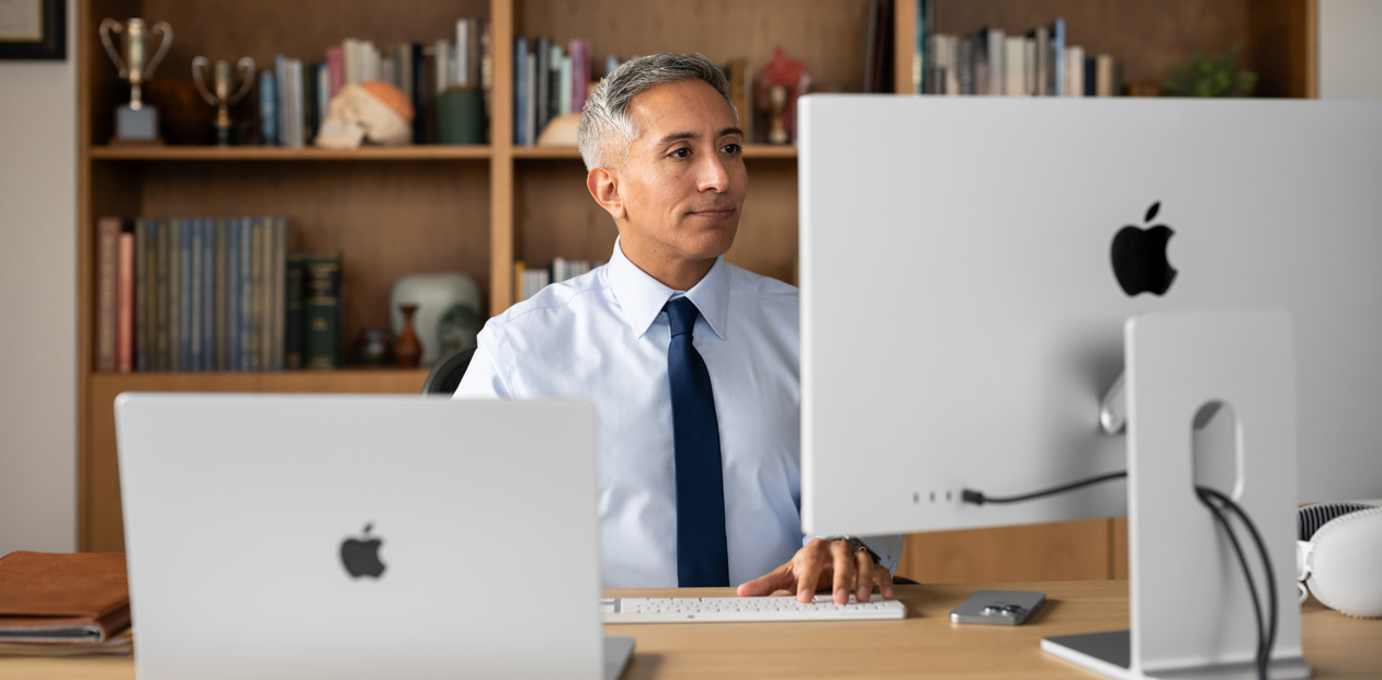 Một nhân viên y tế ngồi ở bàn làm việc, đang nhìn vào iMac và MacBook Pro.