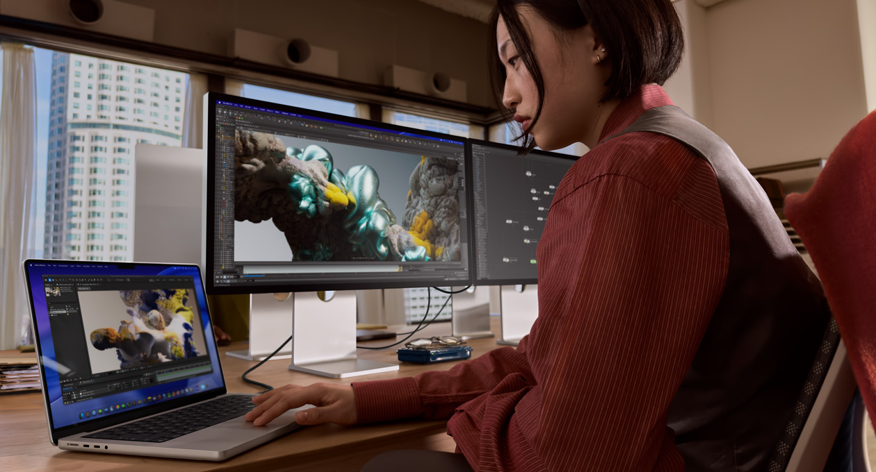 Una persona en una oficina trabaja en una laptop MacBook conectada a un monitor Studio Display XDR mediante un puerto Thunderbolt 5